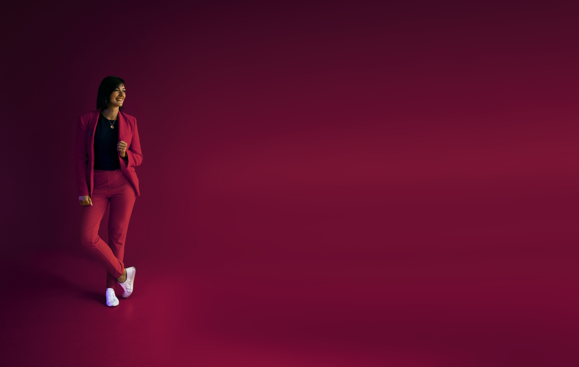 Foodfotografin und Media Awareness Coach Jessica Brach steht lässig vor bordeauxrotem Hintergrund in einem bordeauxrotem Anzug.