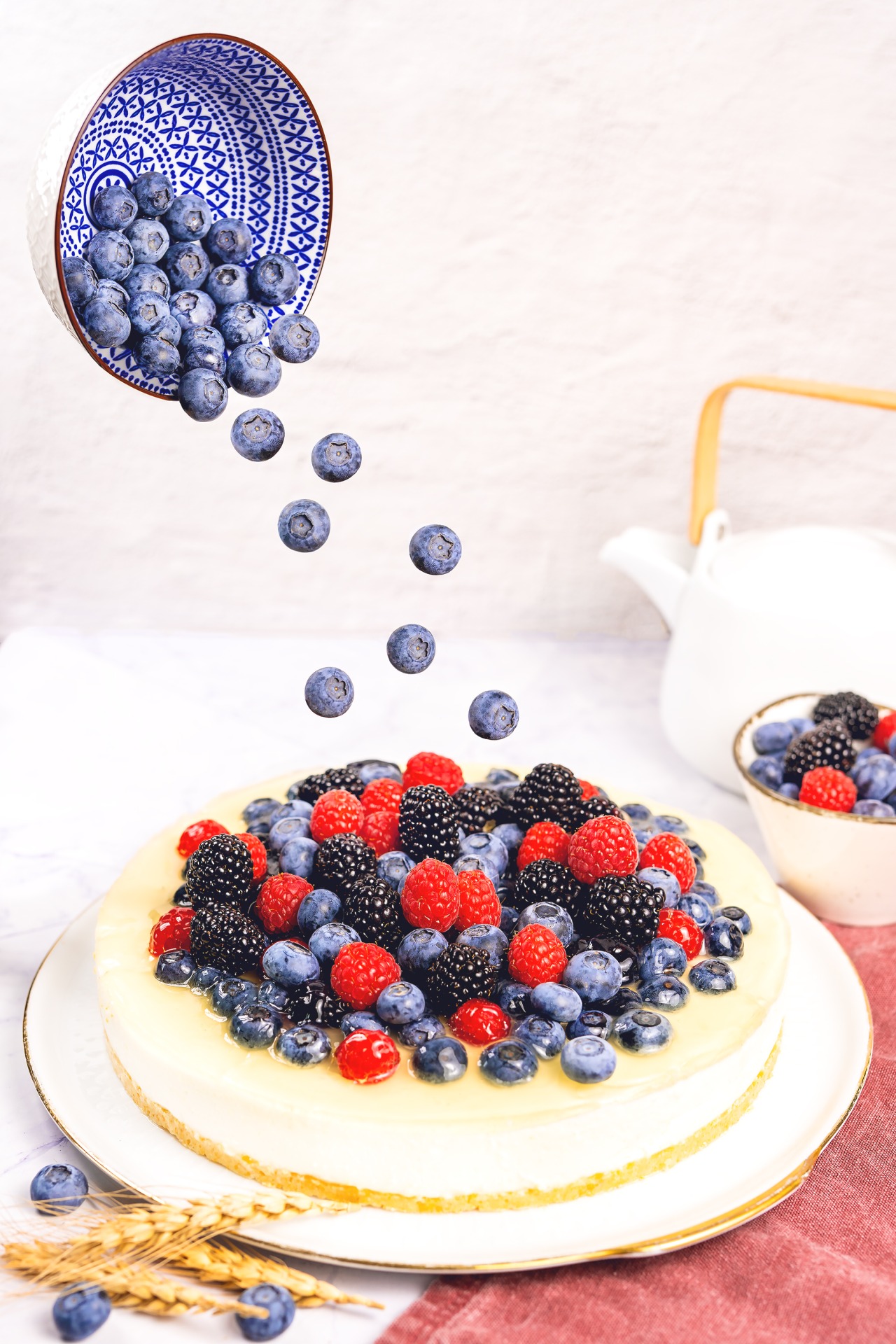 Blaubeeren fallen aus einer ausgekippten Schale, die sich über der Torte befindet, auf die Joghurt-Beeren-Torte hinauf - Foodfotograf